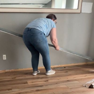 Em pulling baseboard off of a gray wall